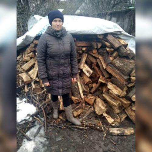 Tetiana standing in front of a pile of firewood
